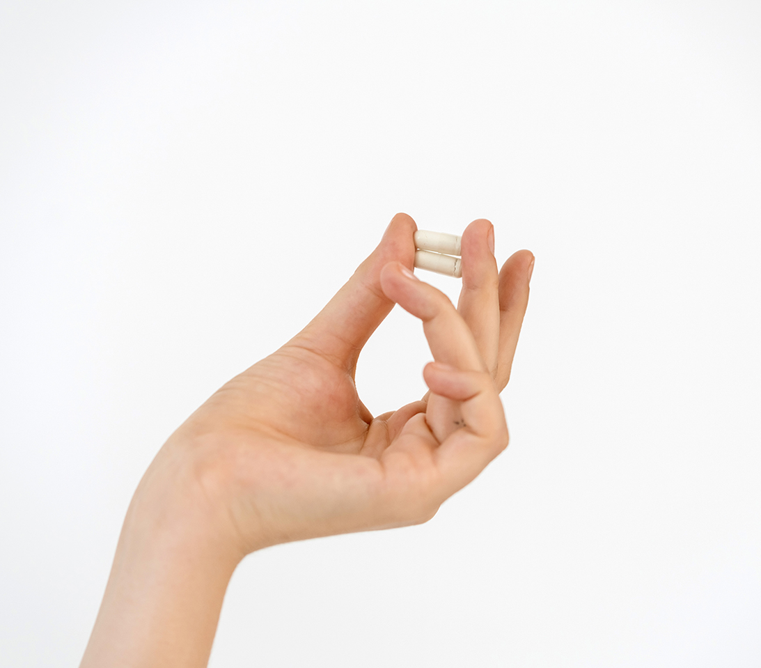 Hand, die zwei Kapseln vor einem schlichten weißen Hintergrund hält, als Symbol für wissenschaftlich fundierte Nahrungsergänzungsmittel.